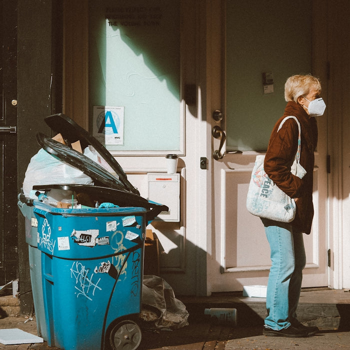 woman in brown jacket and blue denim jeans standing beside red plastic trash bin