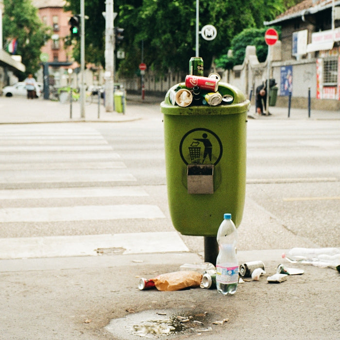 a green trash can sitting on the side of a road