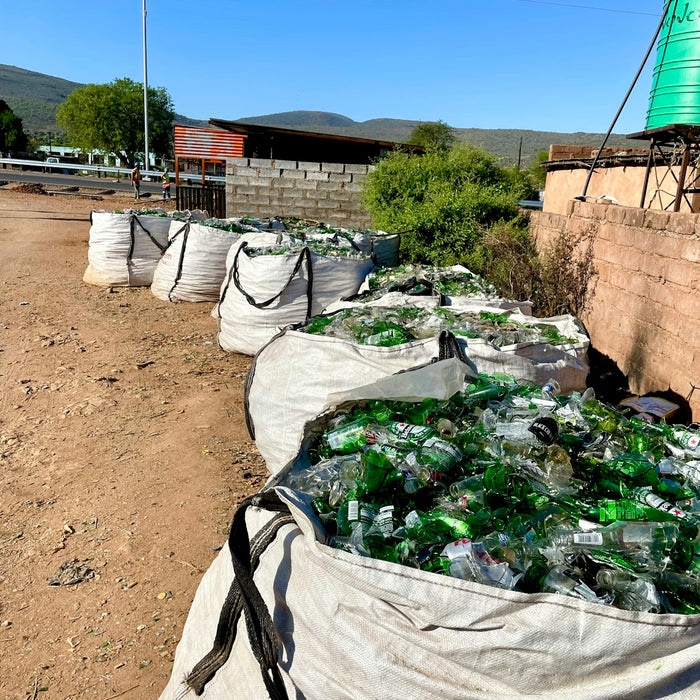 a bunch of bags filled with bottles sitting on top of a dirt field