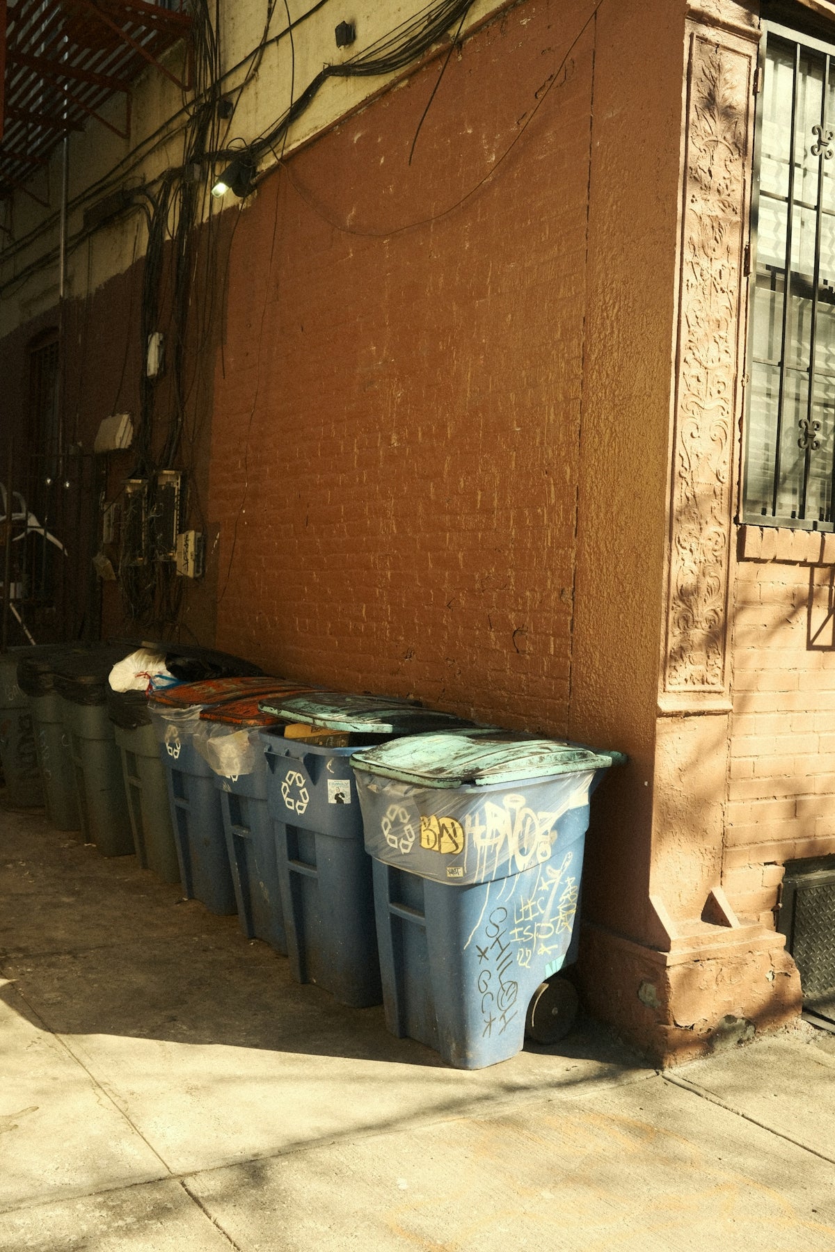 Trash bins are lined up against a brick wall.
