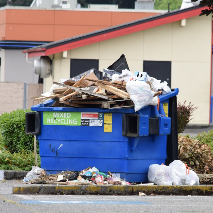 Blue dumpster overflowing with trash and debris.