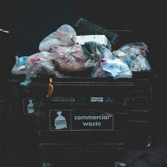 Overflowing commercial waste bin filled with plastic bags.