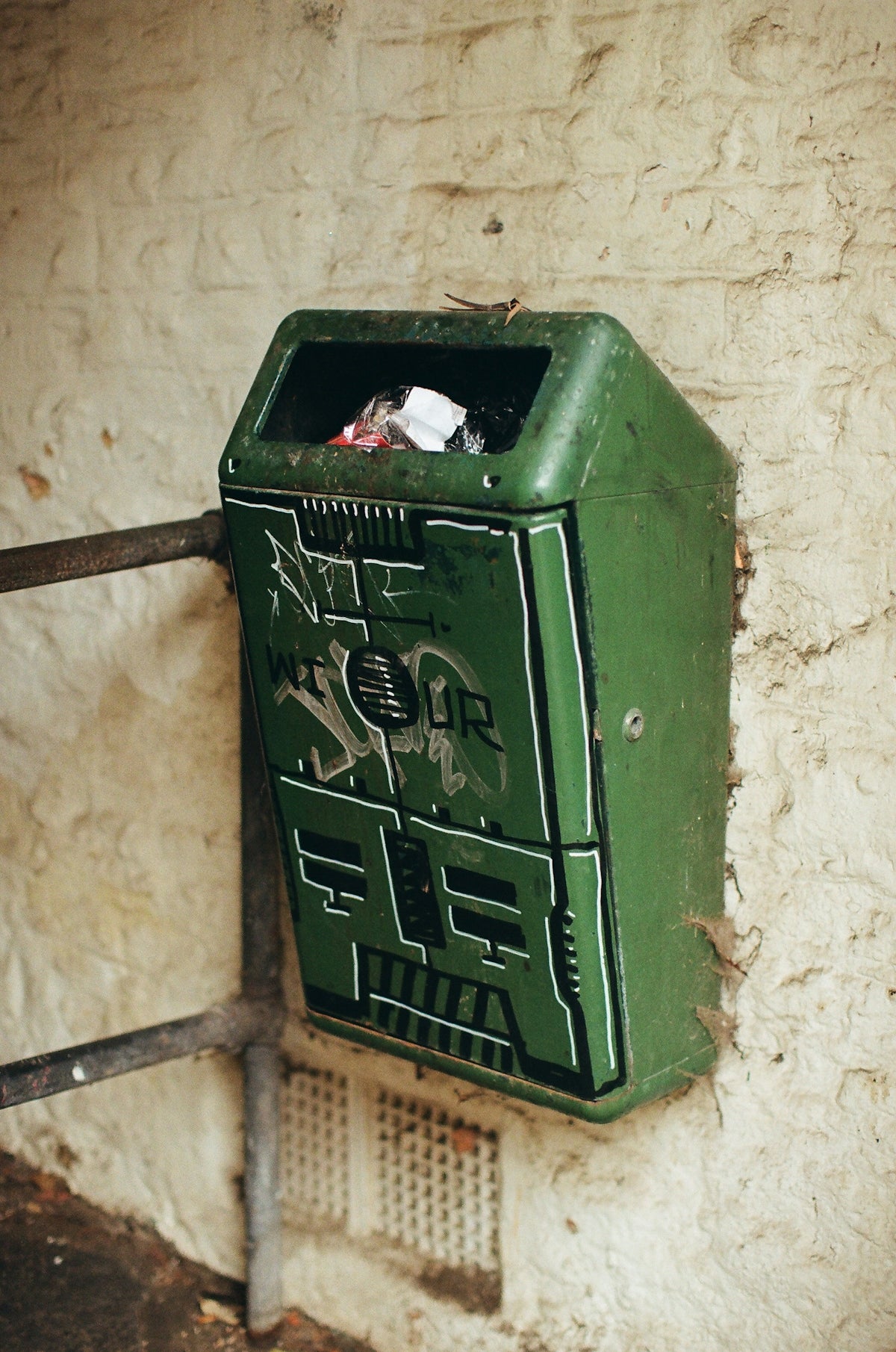 Green trash can with graffiti on wall