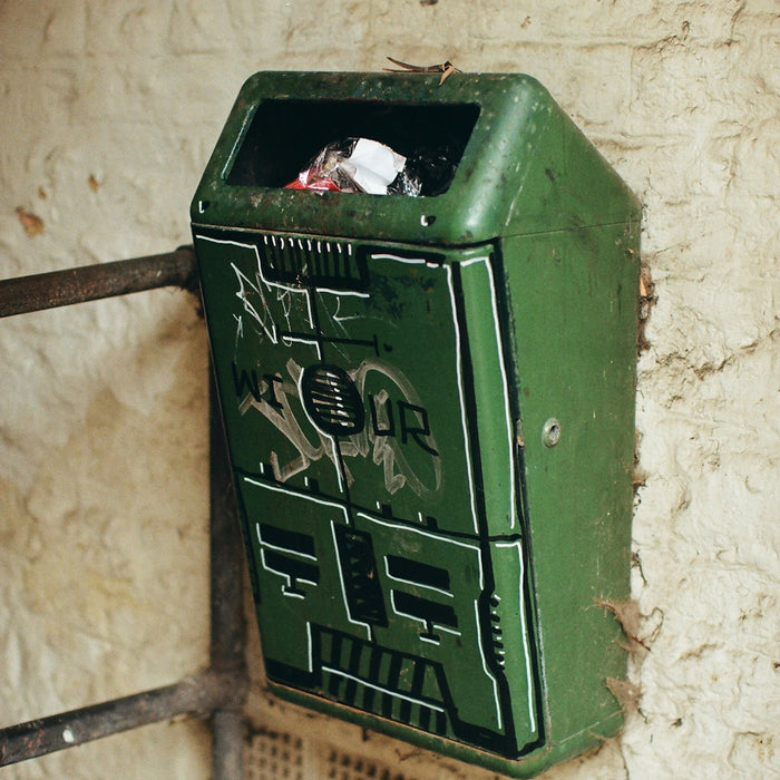 Green trash can with graffiti on wall