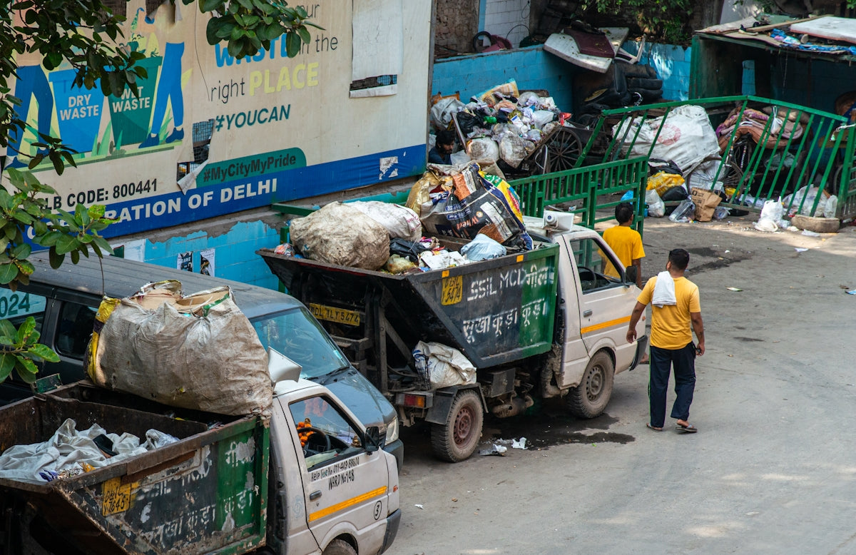 Workers load trash into a garbage truck on a street.