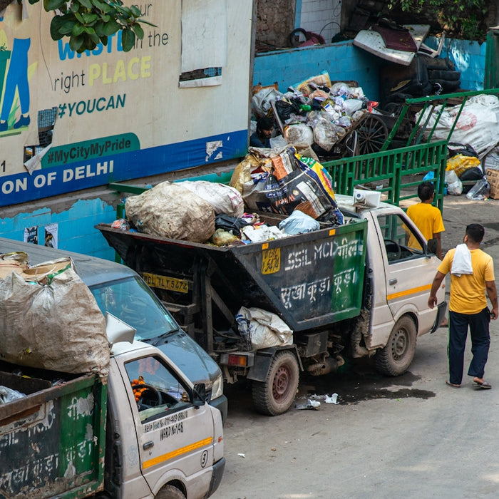 Workers load trash into a garbage truck on a street.