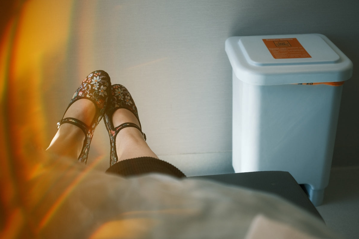 Woman's legs in patterned heels next to a white bin.